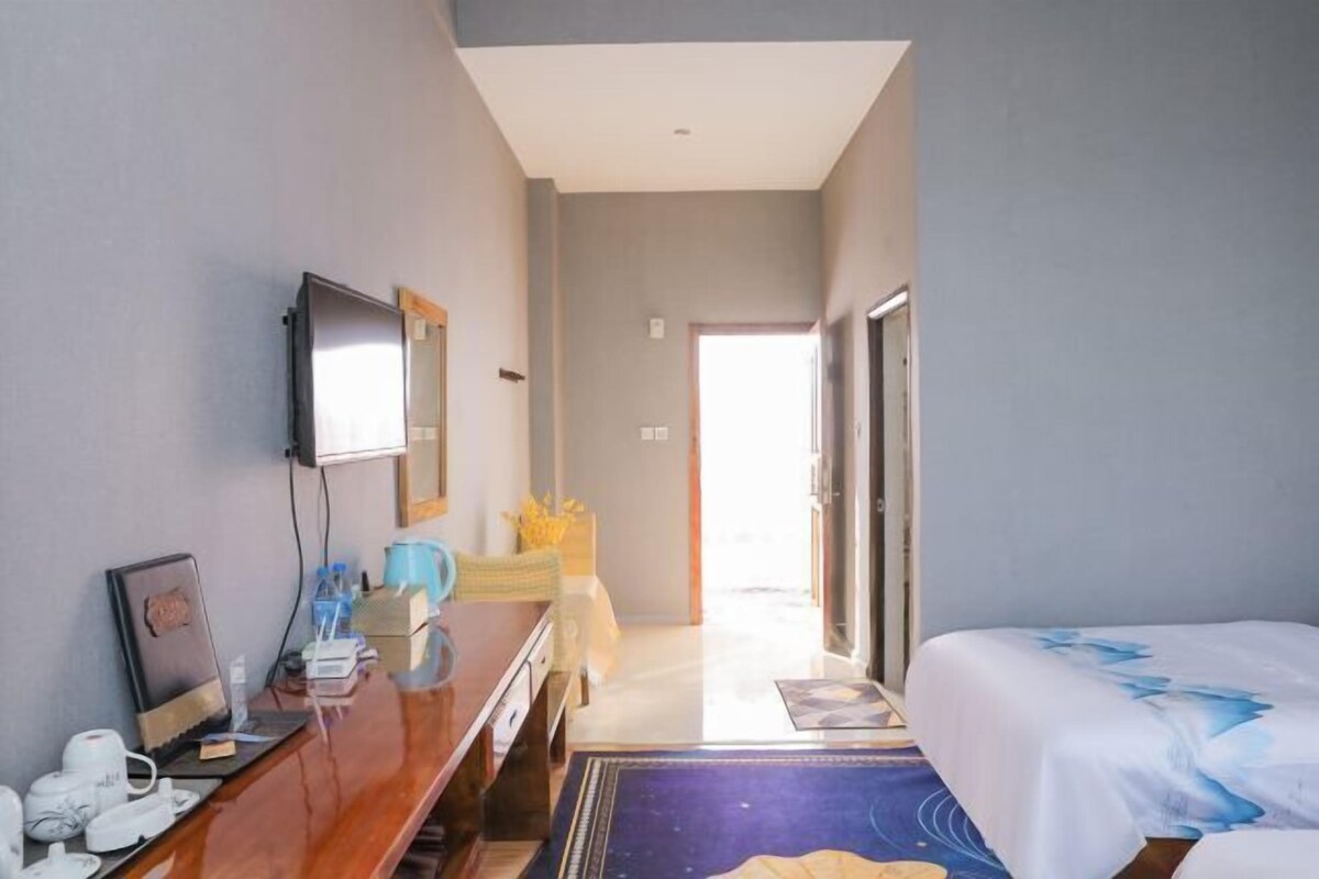 A hotel room with a bed, a desk with a computer, a television, and a bathroom visible through an open door.