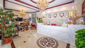 Un hall d’hôtel avec un comptoir d’accueil, des lustres, des plantes en pot et des tableaux encadrés accrochés au mur.
