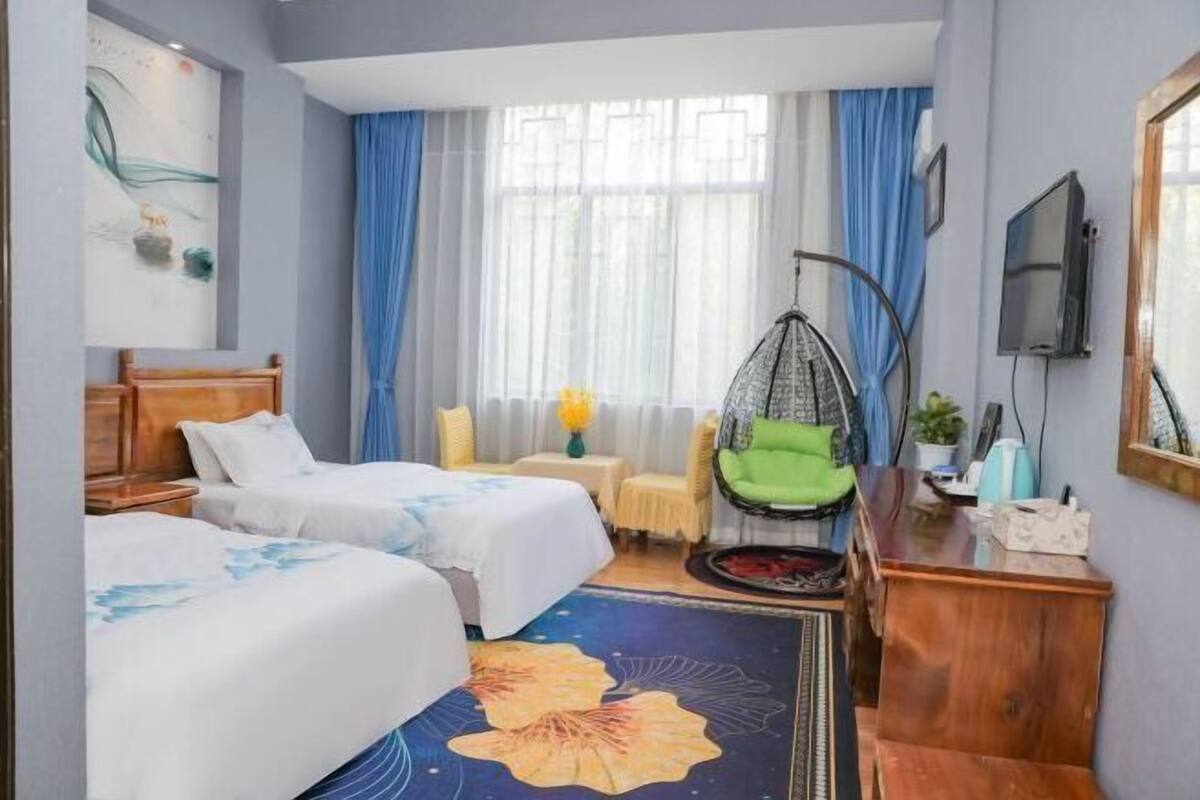 A hotel room with two beds, a desk, a chair, and a television.