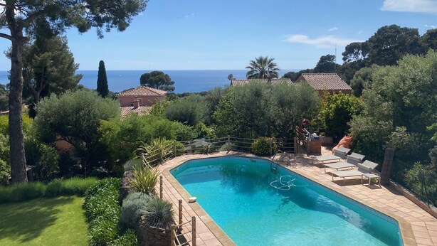 En swimmingpool med utsikt över havet, omgiven av frodig grönska och några få byggnader.