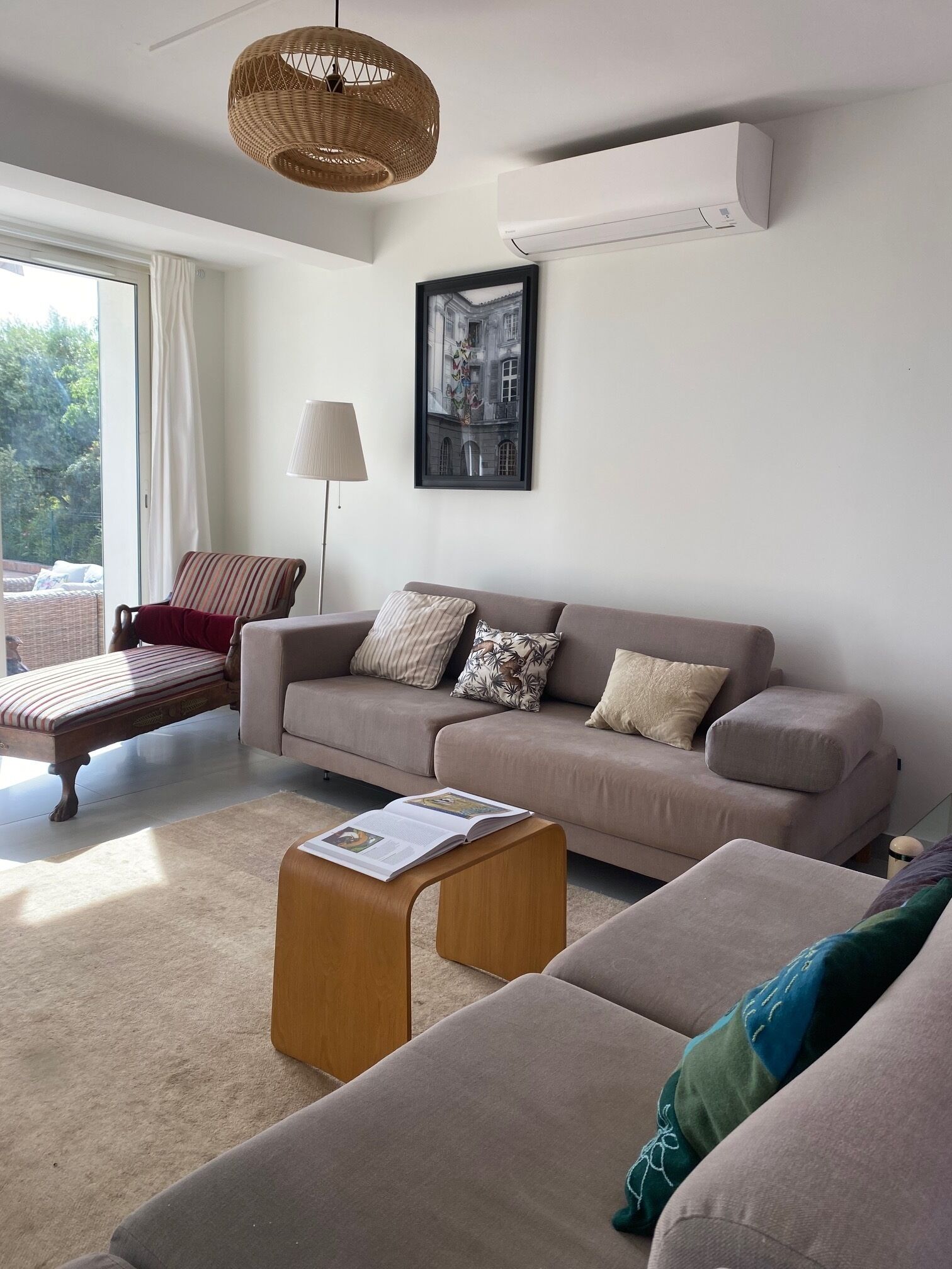 Ein modernes Wohnzimmer mit Sofa, Sitzbank und Couchtisch. Ein gerahmtes Bild hängt an der Wand, und über dem Sofa befindet sich eine Klimaanlage.