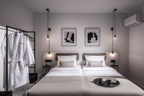 Ein modernes Hotelzimmer mit einem großen Bett, zwei Nachttischen, einem Bademantelständer und einem Kunstwerk an der Wand.