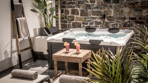 A spa area with a stone wall, a wooden bench, a massage table, and a hot tub with two towels and two drinks. - Icos City 1 a modern apartment centrally located in Hersonissos (Limenas Chersonisou)