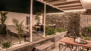 An outdoor dining area with a stone wall backdrop, wooden pergola, and potted plants. - Icos City 1 a modern apartment centrally located in Hersonissos (Limenas Chersonisou)