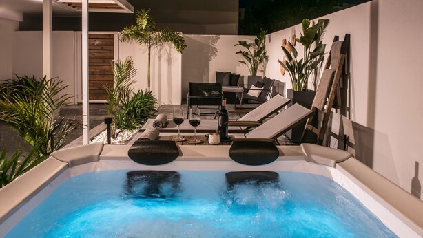 A modern outdoor hot tub area with lounge chairs, a table with wine glasses, and potted plants. - Icos City 1 a modern apartment centrally located in Hersonissos (Limenas Chersonisou)