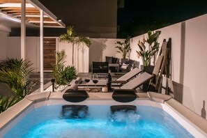 Een modern buitengebied met een hottub, lounge fauteuils, een tafel met wijnglazen en potplanten.