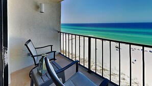 A balcony with two chairs and a table, overlooking a beach with clear blue water and white sand. - Edgewater Tower III #1109 by Resort Collection (Panama City Beach)