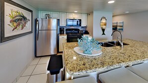 A modern kitchen with granite countertops, stainless steel appliances, and a central island with a decorative coral piece. - Edgewater Tower III #1109 by Resort Collection (Panama City Beach)