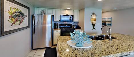 A modern kitchen with granite countertops, stainless steel appliances, and a central island with a decorative coral piece.
