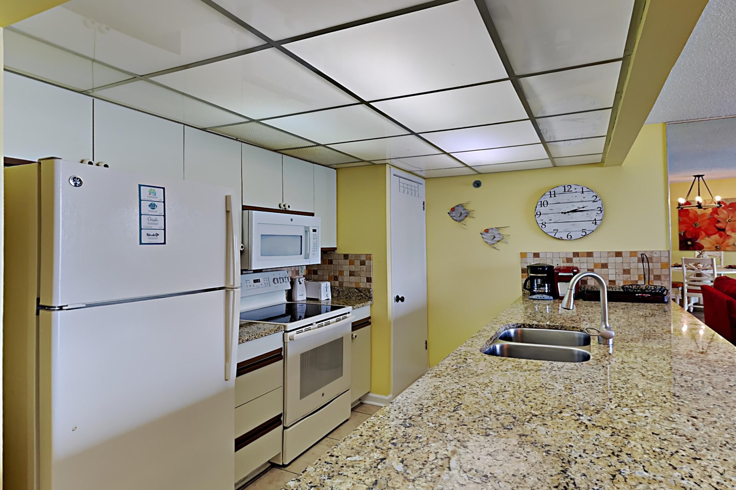 A kitchen with white appliances, a granite countertop, a sink, and a clock on the wall.