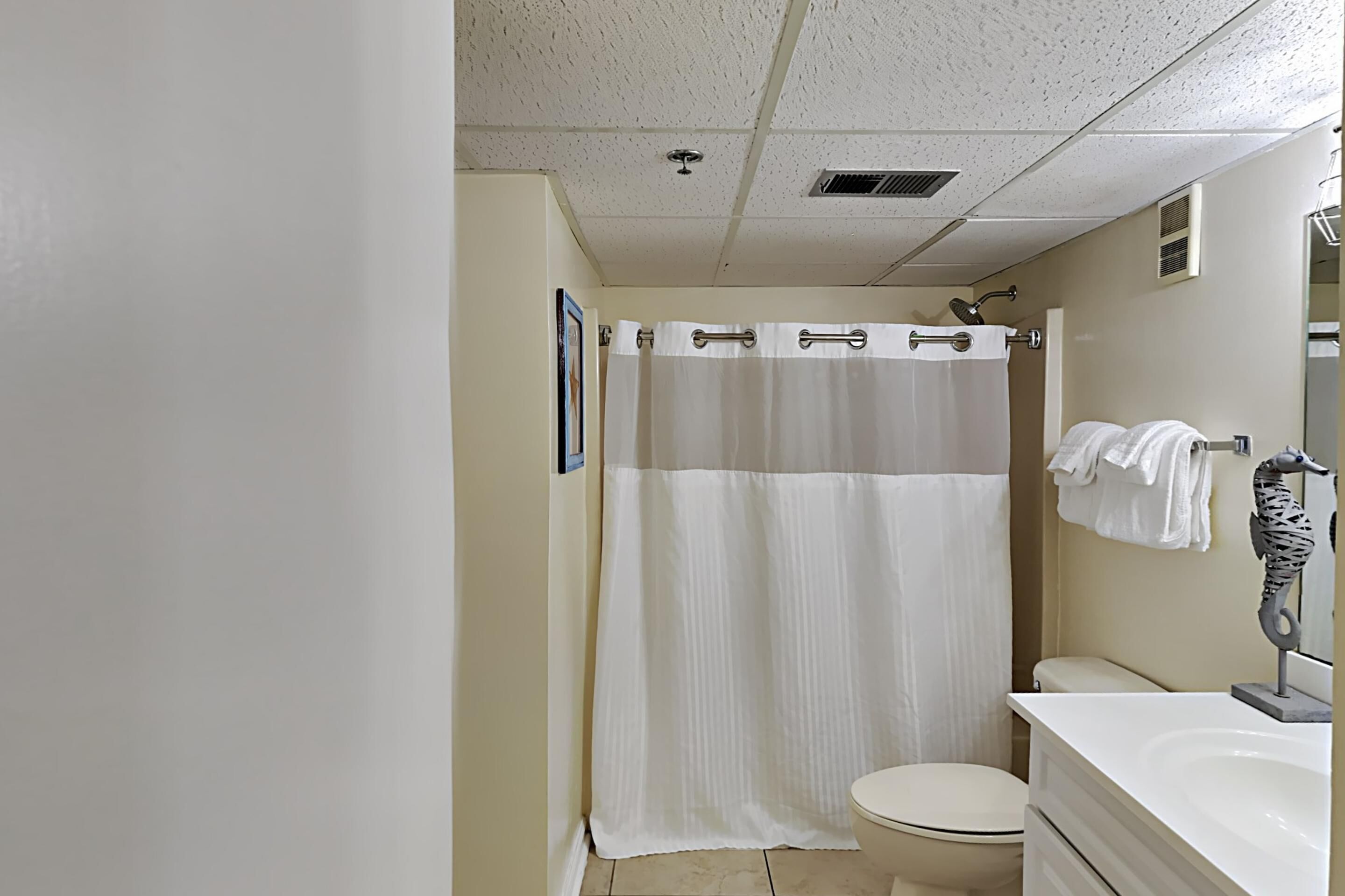 Un baño con cortina de ducha, inodoro y lavamanos con una decoración de caballito de mar.