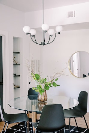 A modern dining area with a glass table, black chairs, a vase with green plants, and a chandelier. - Cation on the Guadalupe (New Braunfels)