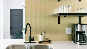 Une cuisine moderne avec un robinet noir, un évier en acier inoxydable et une machine à café posée sur le plan de travail.