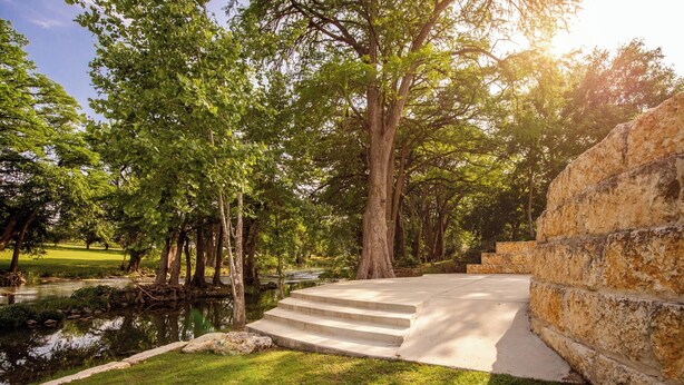 Un parc doté d’un escalier en pierre menant à une plateforme d’observation surplombant un étang, le tout entouré d’arbres et d’herbe.