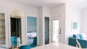 Une pièce moderne avec une table à manger en verre, des chaises bleues, un canapé turquoise et un lit en arrière-plan.