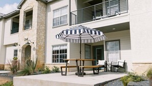Un bâtiment à deux étages avec une façade en pierre, un balcon et un patio comprenant une table de pique-nique et un parasol à rayures.