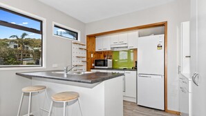 Cozinha moderna com ilha central, armários brancos, micro-ondas e geladeira. Há dois bancos de madeira na ilha.