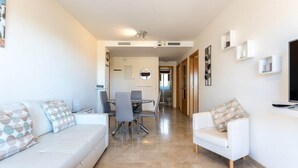 A modern living room with a white sofa, a dining table with chairs, and a TV on the right. - Modernly designed holiday flat in Mijas Costa (La Cala de Mijas)