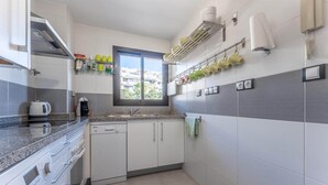 A modern kitchen with white cabinets, a granite countertop, a built-in dishwasher, and a window providing natural light. - Modernly designed holiday flat in Mijas Costa (La Cala de Mijas)