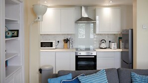 A compact kitchen with white cabinets, a built-in oven, a microwave, and a kettle. - Swan Cove Gourock 1 bedroom apartment (Gourock)