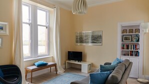 A living room with a sofa, a bench, a television, and a bookshelf. - Swan Cove Gourock 1 bedroom apartment (Gourock)