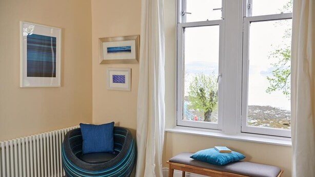 A room with a large window, a round bean bag chair, a wooden bench, and framed pictures on the wall. - Swan Cove Gourock 1 bedroom apartment (Gourock)