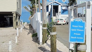 Un letrero que indica acceso privado a la playa, una valla de madera y un edificio con fachada azul.