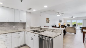 Una cocina moderna con gabinetes blancos, encimeras de granito y electrodomésticos de acero inoxidable.