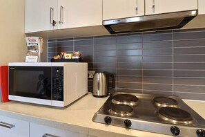 A kitchen with a white microwave, a stainless steel stove, and a kettle on the counter.