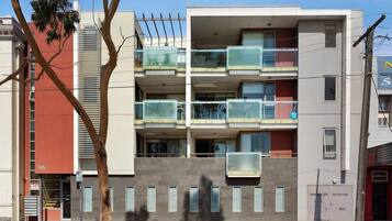 A multi-story residential building with balconies, a visible entrance, and a sign for a sprinkler booster.