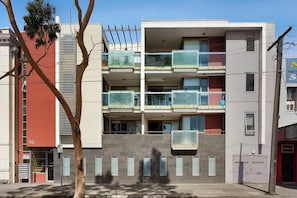 Un edificio residencial de varios pisos con balcones, una entrada visible y un cartel para un impulsor de aspersores.