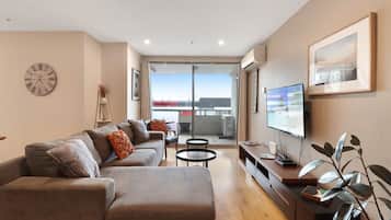 A modern living room with a sofa, a flat-screen TV, a coffee table, and a balcony with a view.