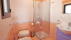 Een badkamer met een douche met glazen wand, toilet, bidet en wastafel.