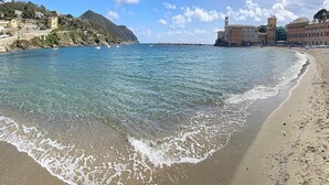 A coastal scene with a sandy beach, clear blue water, and buildings along the shore.