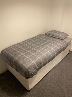 Simple, functional space with a single bed and grey carpet.
