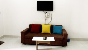 A living room with a brown sofa, three colorful cushions, a white coffee table, and a mounted TV. - Call Sea Nha Trang  (Nam Nha Trang)
