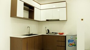 A compact kitchen with wooden cabinets, a white countertop, a sink, a kettle, and a refrigerator. - Call Sea Nha Trang  (Nam Nha Trang)