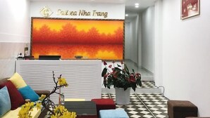 A reception area with a checkered floor, a sofa with colorful cushions, a potted plant, and a large wall-mounted sign. - Call Sea Nha Trang  (Nam Nha Trang)
