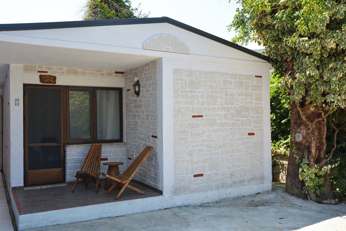 Ein kleines Gebäude mit einer Veranda, zwei Holzstühlen und einem Tisch.
