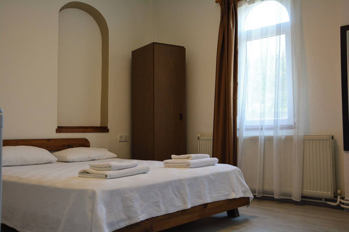 Ein Schlafzimmer mit Bett, Kleiderschrank, Heizkörper und einem Fenster mit Vorhängen.