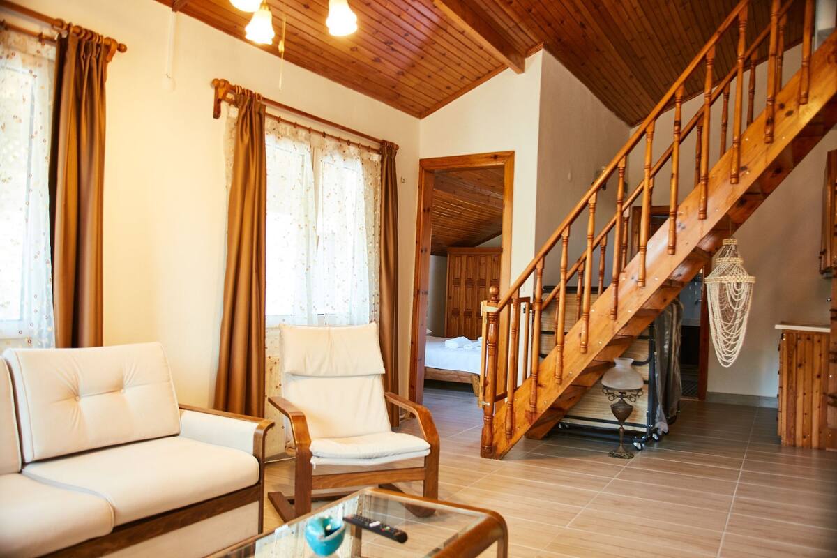 Ein großzügiger Wohnbereich mit einer Holztreppe, einem Sofa, einem Sessel und einem Tisch mit Fernbedienung.