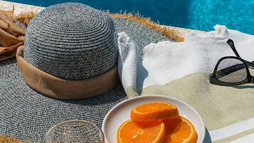Cenário à beira da piscina com chapéu de palha, um prato de laranjas, um copo d'água e um par de óculos de sol.