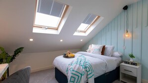 A bedroom with a skylight, a bed with decorative pillows, a bedside table with books, and a plant. - All Ensuite,smarttvs,garden,20 Mins to Nec,parking (Coventry)