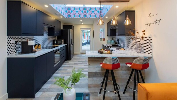 A modern kitchen with dark cabinetry, a central island, and bar stools. - All Ensuite,smarttvs,garden,20 Mins to Nec,parking (Coventry)