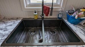 A kitchen sink with a faucet, a dish soap bottle, and a blue container with utensils. - Little Yellow Cottages #3 (Port Austin)