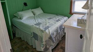 A small, green-walled bedroom with a single bed, a nightstand, and a window with blinds. - Little Yellow Cottages #3 (Port Austin)