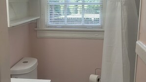 Un baño pequeño con inodoro, lavamanos, cortina de ducha y ventana con persianas.