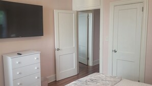 Un dormitorio con cama, cómoda, televisor y dos puertas que dan a otras habitaciones.