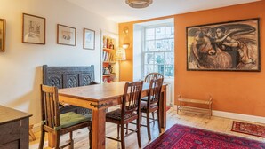 Un'area pranzo con un tavolo e sedie in legno, una panca, una libreria e un quadro grande appeso al muro.