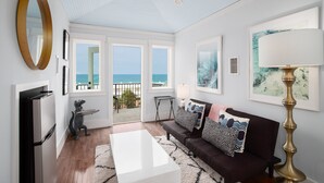 Ein modernes Wohnzimmer mit Meerblick, einem schwarz-weißen Couchtisch, einem braunen Sofa mit gemusterten Kissen und einem großen Spiegel an der Wand.
